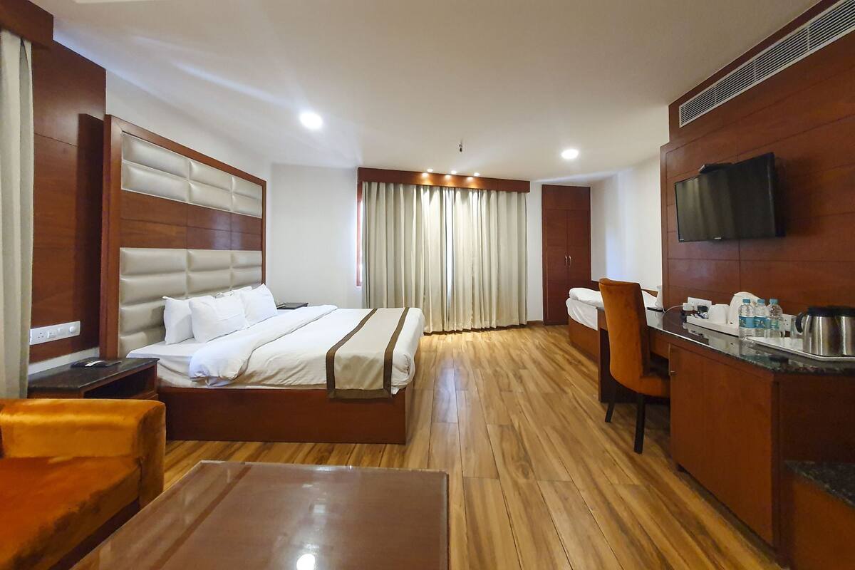 A hotel room with a bed, a desk, a chair, a TV, and a minibar.