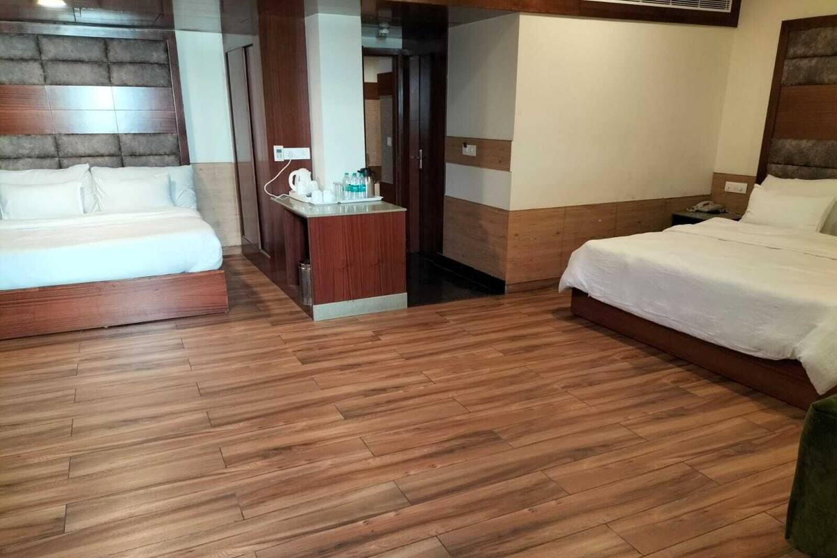 A hotel room with two beds, a wooden floor, a small desk with a chair, and a door leading to another room.