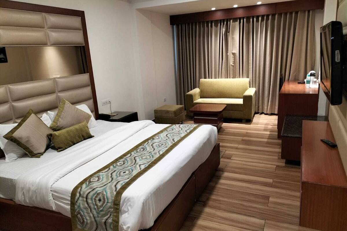 A hotel room with a large bed, a sofa, a small table, and a TV.