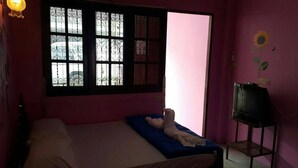 A room with a bed, a TV on a stand, and a window with decorative bars. - PKhotelresort (Prachin Buri)
