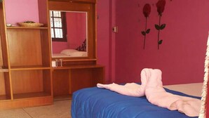 A bedroom with a bed, a wooden wardrobe, a pink wall, and a blue rug. - PKhotelresort (Prachin Buri)