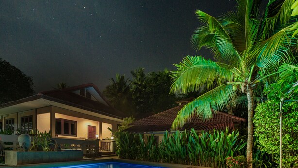 A nighttime view of a resort with a swimming pool, palm trees, and a building with a tiled roof. - Samui Green Space Resort (Koh Samui)