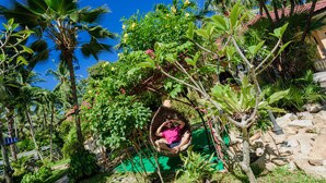 A person relaxing in a wicker swing chair amidst lush greenery and a stone wall. - Samui Green Space Resort (Koh Samui)