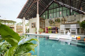 A pool area with a covered seating area, chairs, and potted plants. - Villa De Van (Da Nang)