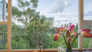Vista a través de una ventana con un jarrón de flores, una tetera y una bandeja con tazas.