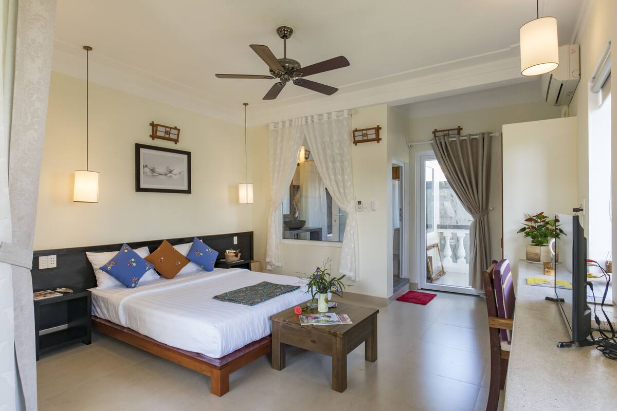 A hotel room with a bed, bedside tables, a ceiling fan, a TV, and a view of the outside.