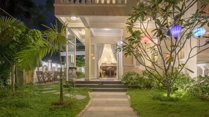 Un sendero bien iluminado que lleva a un edificio, donde se ve un comedor a través de las puertas de vidrio.