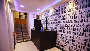 Zona de recepción con un mostrador negro, un reloj y un muro con diseño.