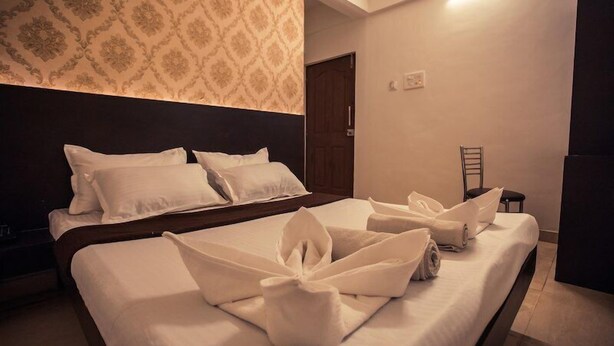 Una habitación de hotel con una cama bien hecha, cabecera, pared con papel tapiz estampado y una puerta.