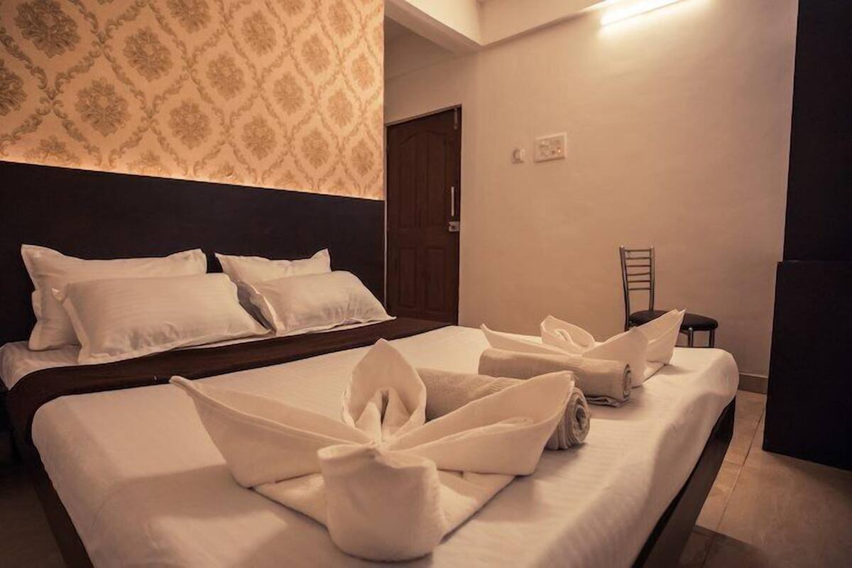 Quarto de hotel com cama bem arrumada, cabeceira, parede com papel de parede estampado e uma porta.