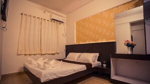 Una habitación de hotel con una cama, una mesita de noche, un espejo y una ventana con cortinas.