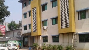 Un edificio de varios pisos con fachada amarilla y múltiples ventanas. Hay plantas en macetas a lo largo de la fachada y una escalera apoyada contra el edificio.
