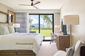 A hotel room with a bed, a desk, a chair, a TV, and a large window with a view of palm trees and hills. - Timbers Kauai (Lihue)