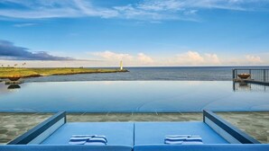 A poolside view with lounge chairs and a view of the ocean and a lighthouse. - Timbers Kauai (Lihue)