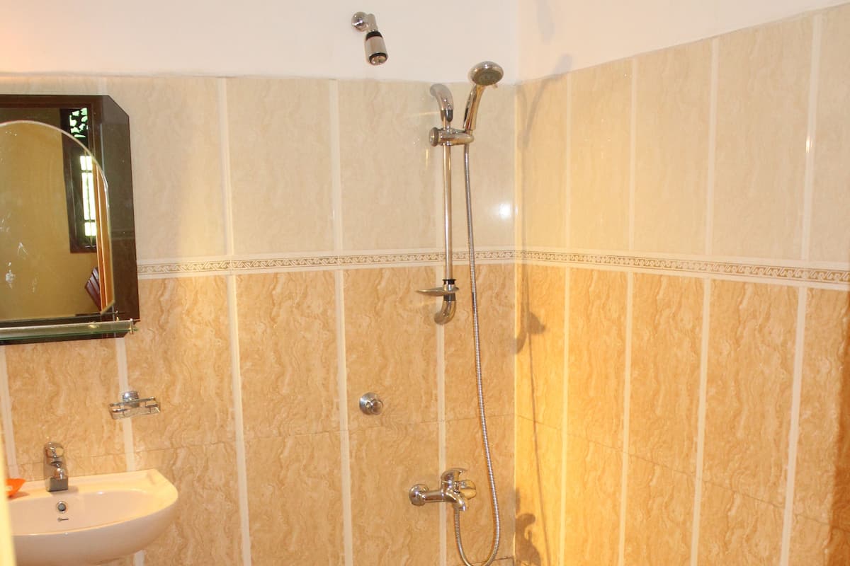 A bathroom with a sink, toilet, shower, and a small window.