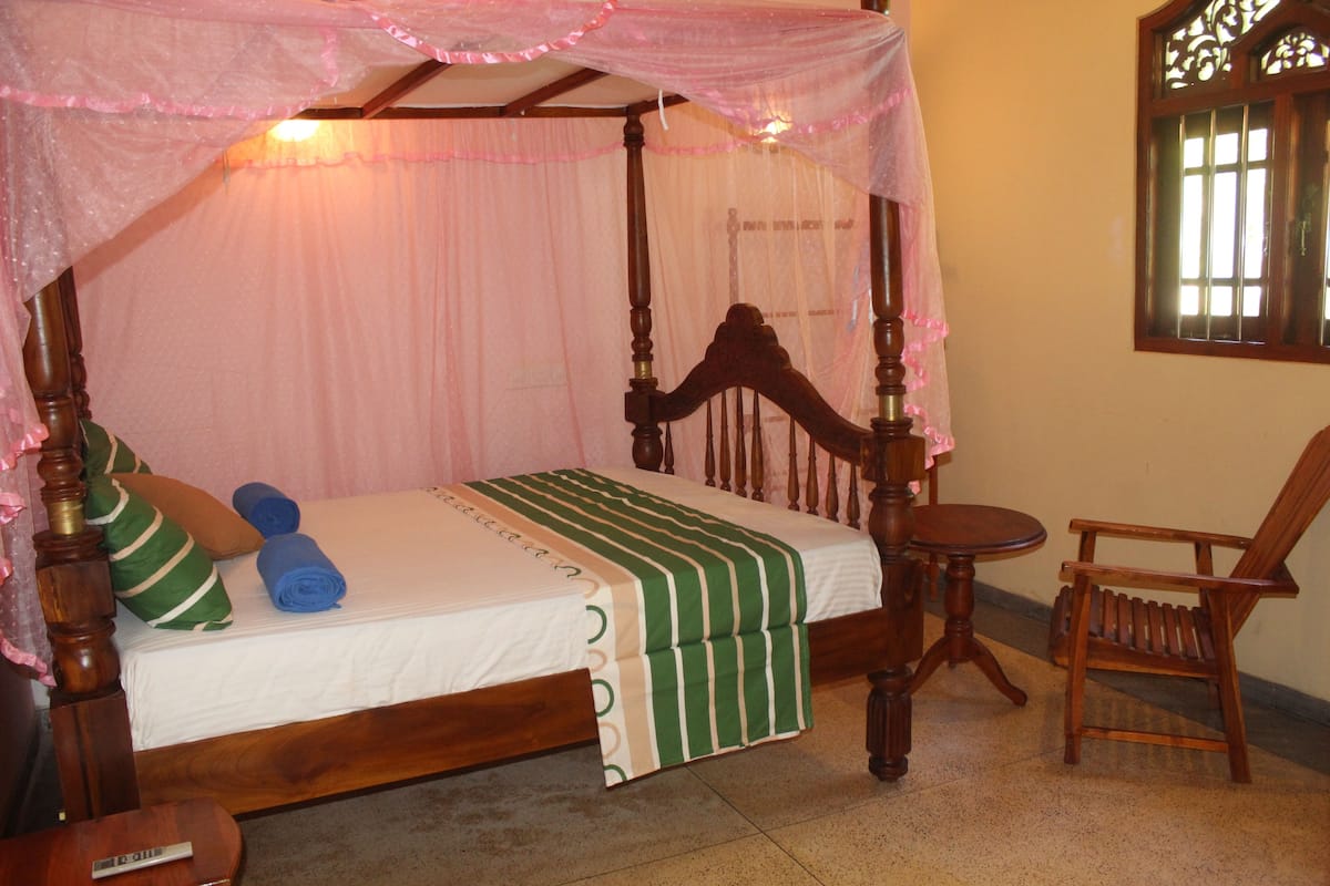 A four-poster bed with a canopy, a wooden chair, and a small table.