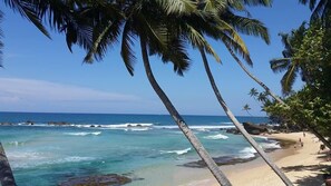 A beach with clear blue water, palm trees, and rocky outcrops. - Tiny Royal Palace (Unawatuna)