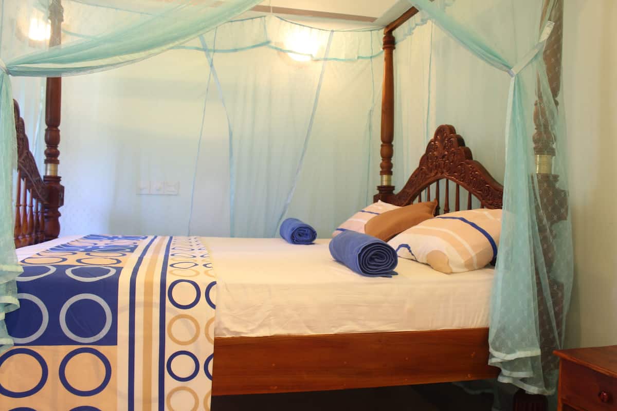 A four-poster canopy bed with a patterned bedspread, a wooden headboard, and a nightstand to the right.