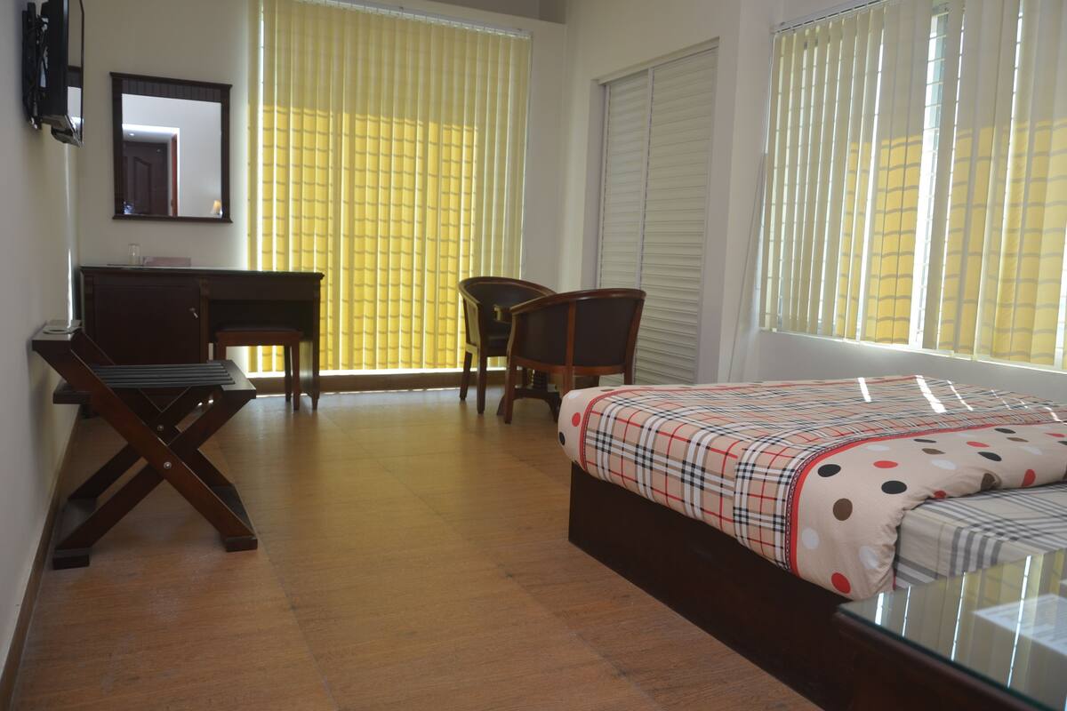 A bedroom with a bed, a desk, a chair, and a window with blinds.