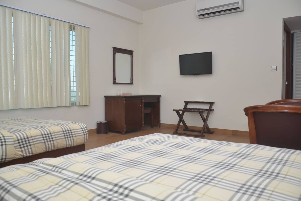 A hotel room with two beds, a desk, a chair, a television, and a window with blinds.
