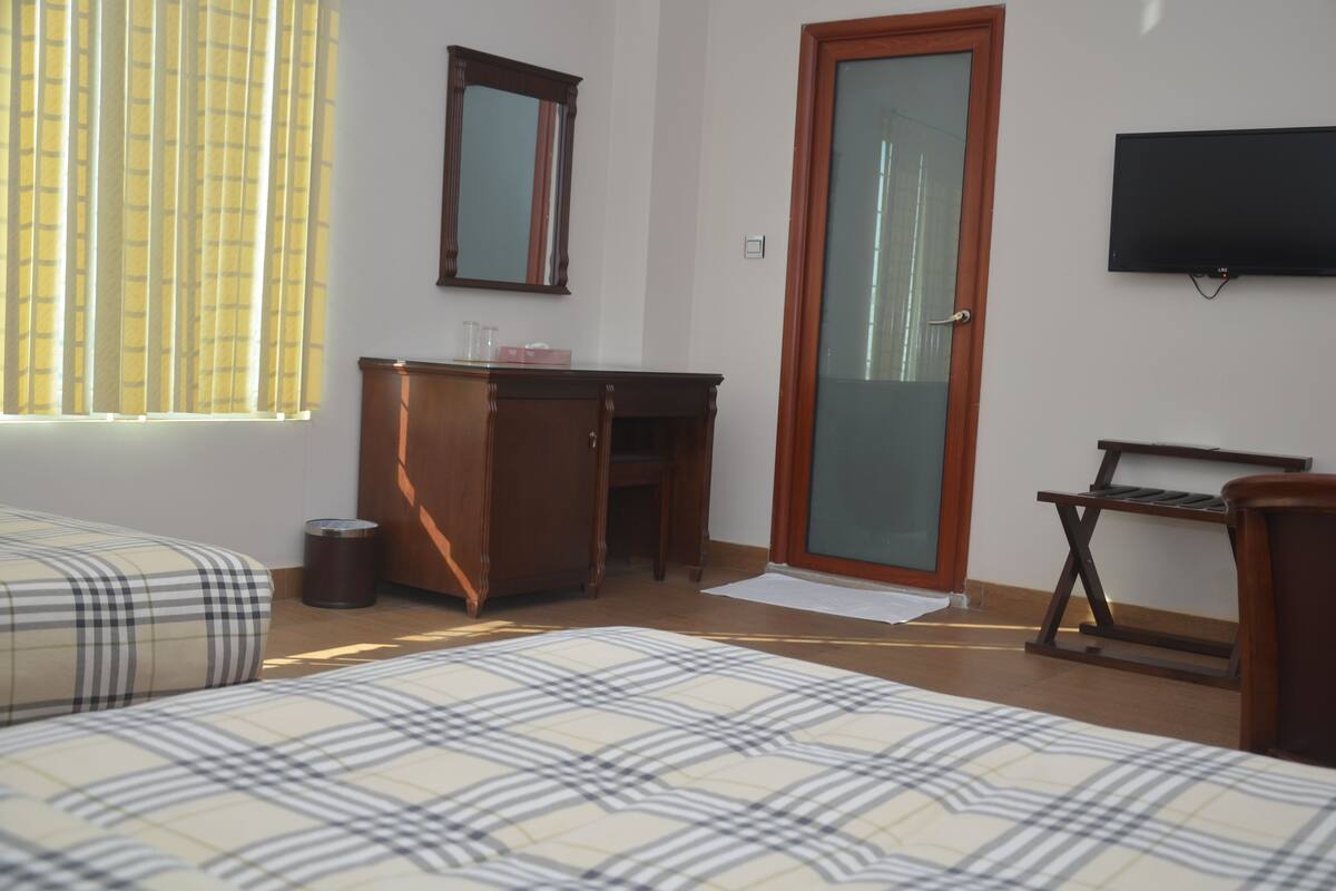 A hotel room with a bed, a desk, a mirror, a television, and a window with curtains.