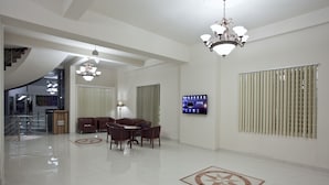 Un hall d’entrée spacieux avec un plafond haut, un lustre, un téléviseur fixé au mur et un coin salon avec une table et des chaises.