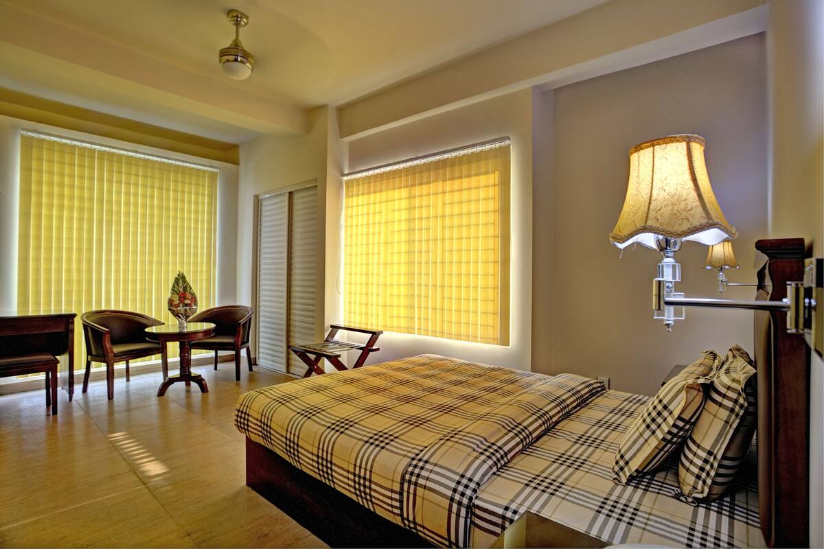 A hotel room with a bed, two chairs, a small table, and a lamp.