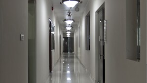 Un long couloir étroit, doté d’un sol ciré et d’une rangée de portes d’un seul côté.
