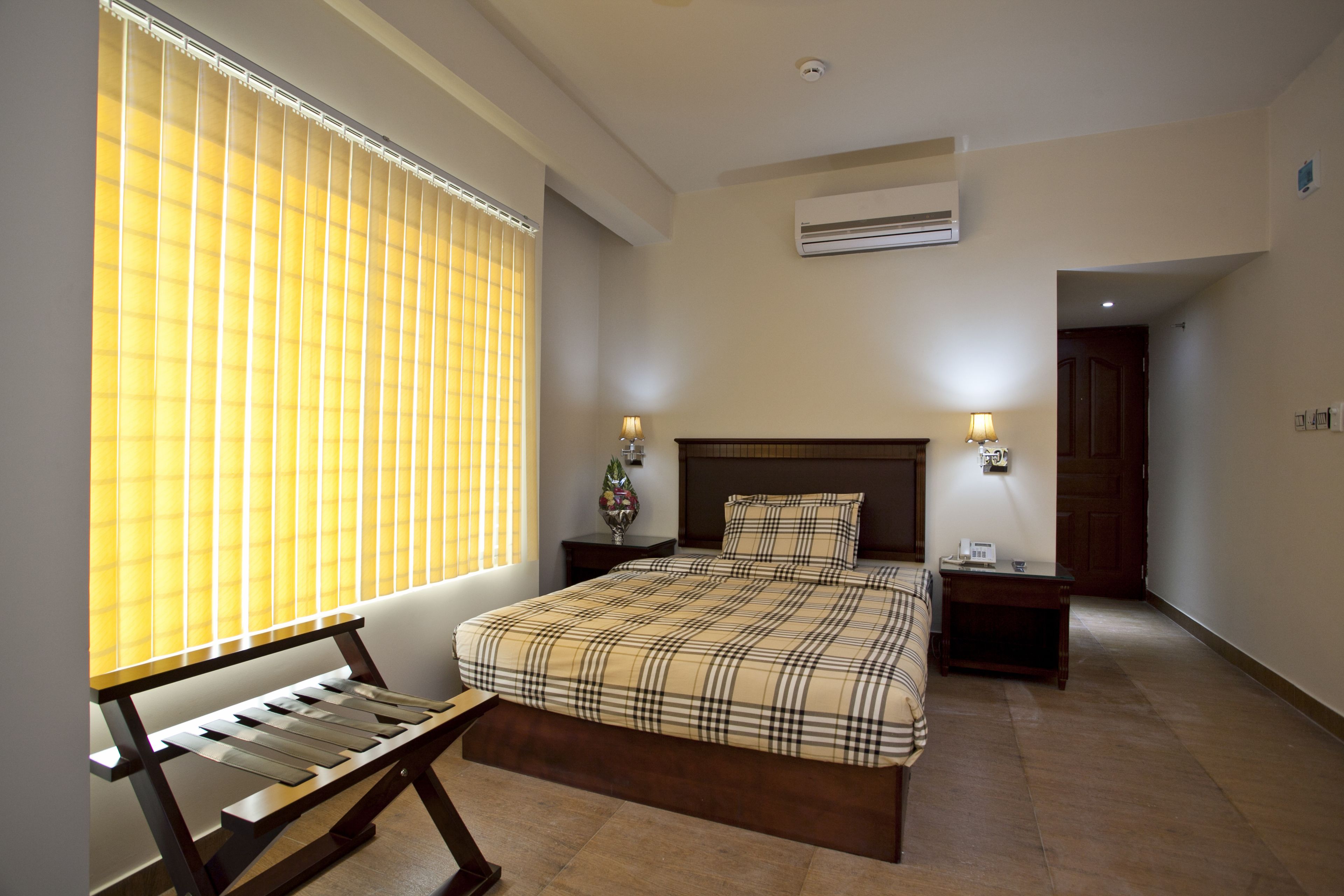 A bedroom with a bed, bedside lamps, a bench, and a window with blinds.