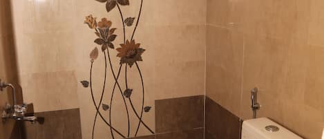 Et badeværelse med toilet, bruser og et dekorativt blomstermønster på væggen.