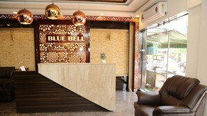 Un área de recepción con mostrador de mármol, sofá de cuero y una pared decorativa con el nombre 'BLUE BELL'.