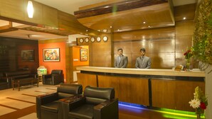 A hotel reception area with leather chairs, a reception desk, and two men standing behind it. - Rafflesia Serviced Apartments (Dhaka)
