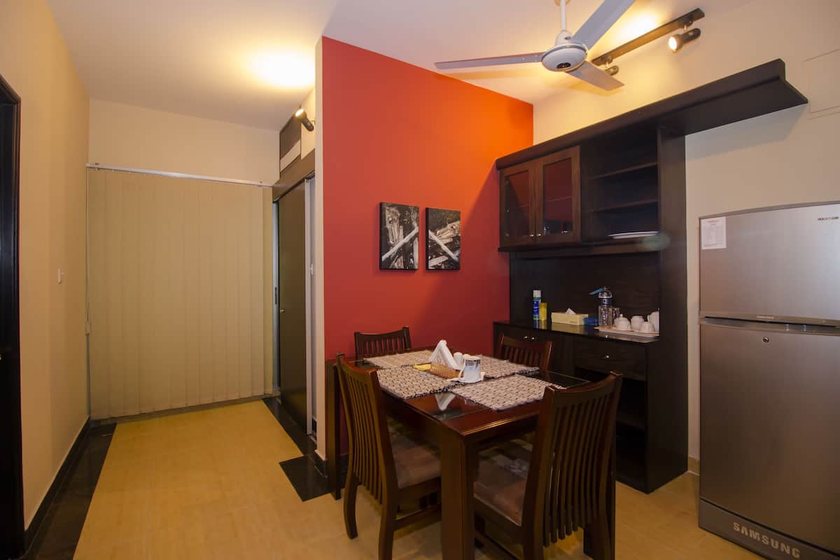 A compact kitchen with a refrigerator, wooden dining table, chairs, and a ceiling fan.