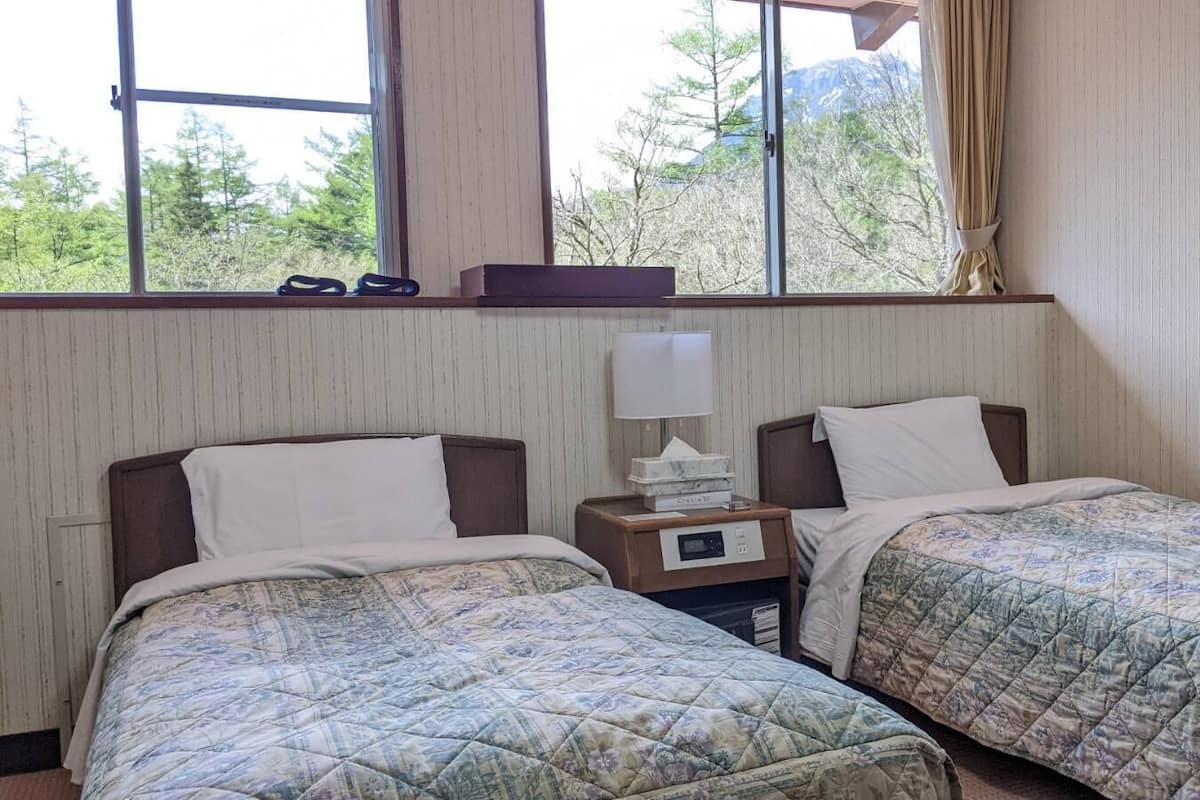 Une chambre avec deux lits, une table de chevet avec une lampe et une fenêtre donnant sur des arbres et des montagnes.