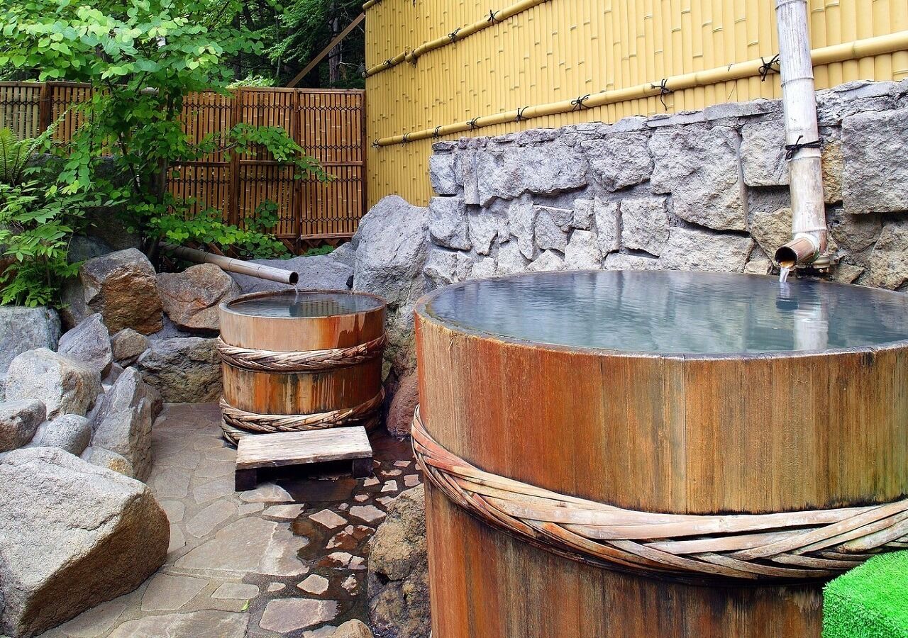 En traditionel japansk onsen med badekar af sten og træ, et bambushegn og en stenvæg.