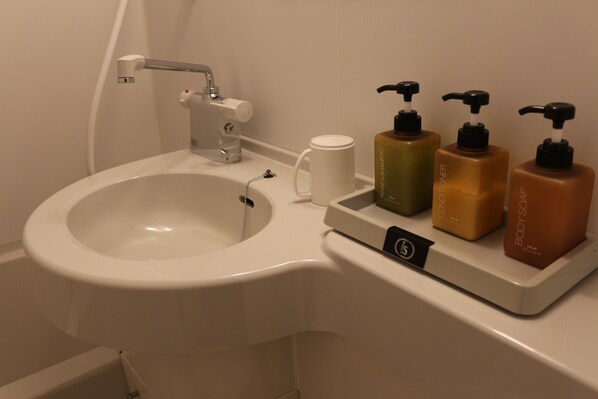 A bathroom sink with a faucet, a cup, and three soap dispensers. - Pension Asangi (Hachimantai)