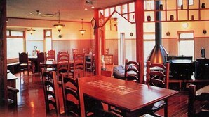 A restaurant with wooden tables and chairs, a fireplace, and large windows. - Pension Asangi (Hachimantai)