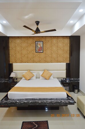 A modern hotel room with a large bed, a ceiling fan, a nightstand, and a wall-mounted picture.