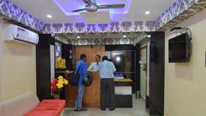 A reception area with a ceiling fan, a reception desk, a red sofa, and a wall-mounted TV. - Hotel Biswanath (Guwahati)