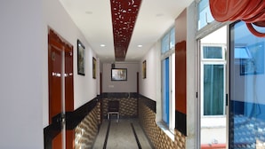 A hallway with a tiled floor, wooden doors, and a view of the outside through a large window. - Hotel Biswanath (Guwahati)
