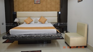 A modern hotel room with a large bed, a bedside table, a chair, and a decorative wall panel. - Hotel Biswanath (Guwahati)