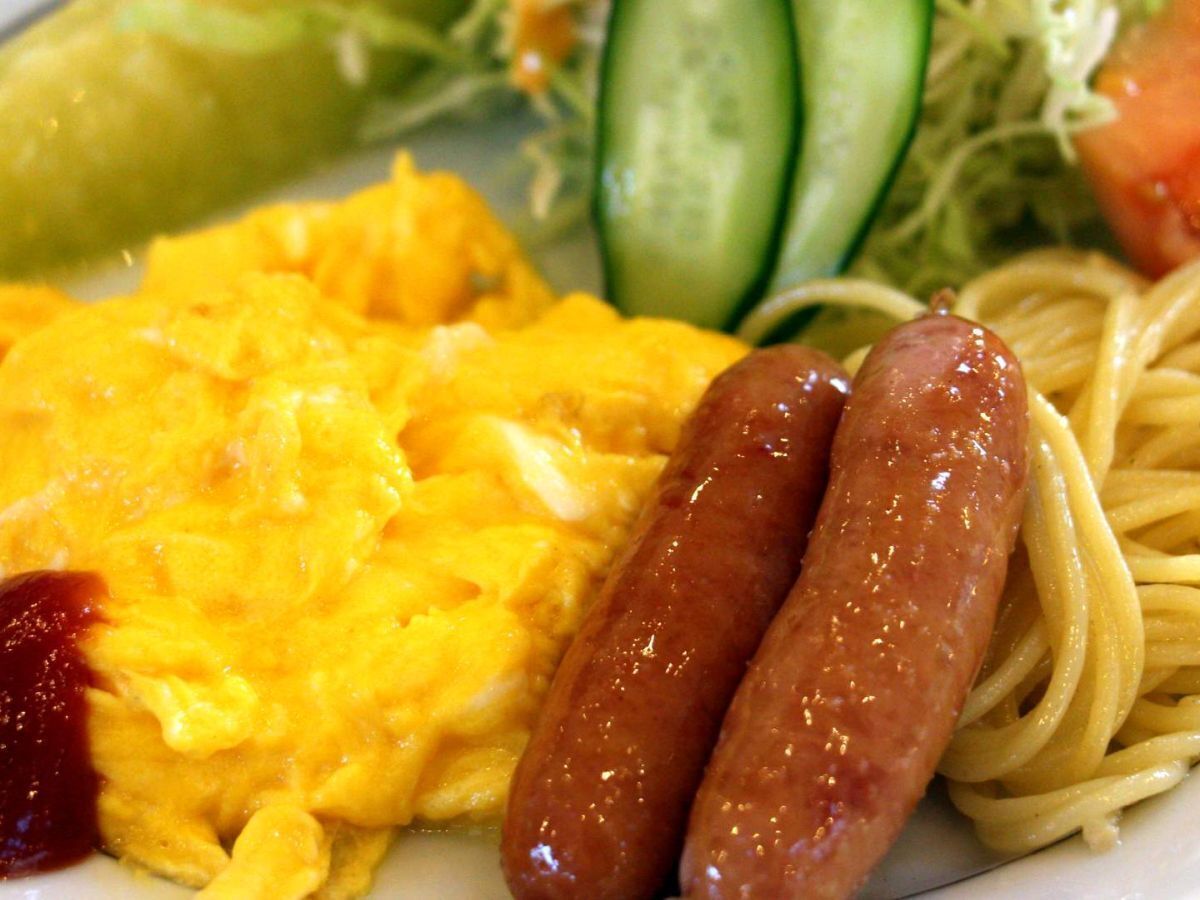A plate with scrambled eggs, sausages, spaghetti, and a side salad.