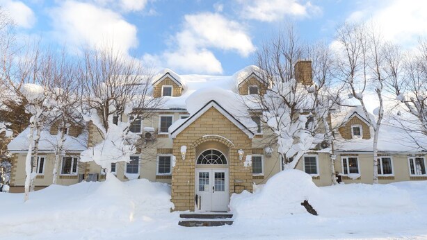 Una casa grande de varios pisos con fachada simétrica, una entrada central con arco decorativo y un entorno cubierto de nieve.