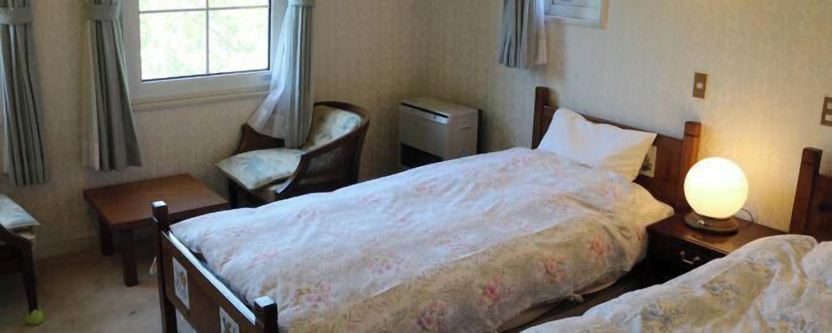 A bedroom with a bed, bedside table, chair, and a lamp.
