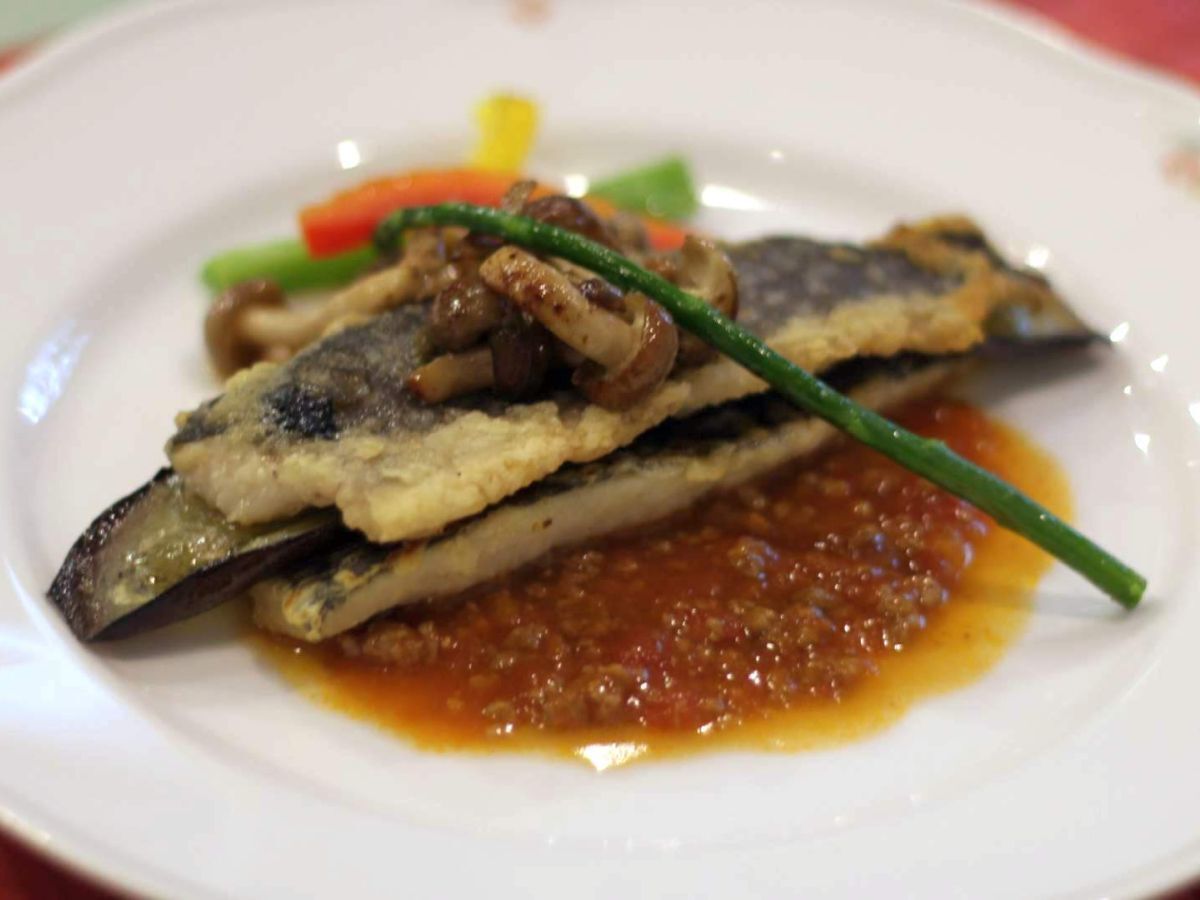 A plate with grilled fish, vegetables, and a sauce.