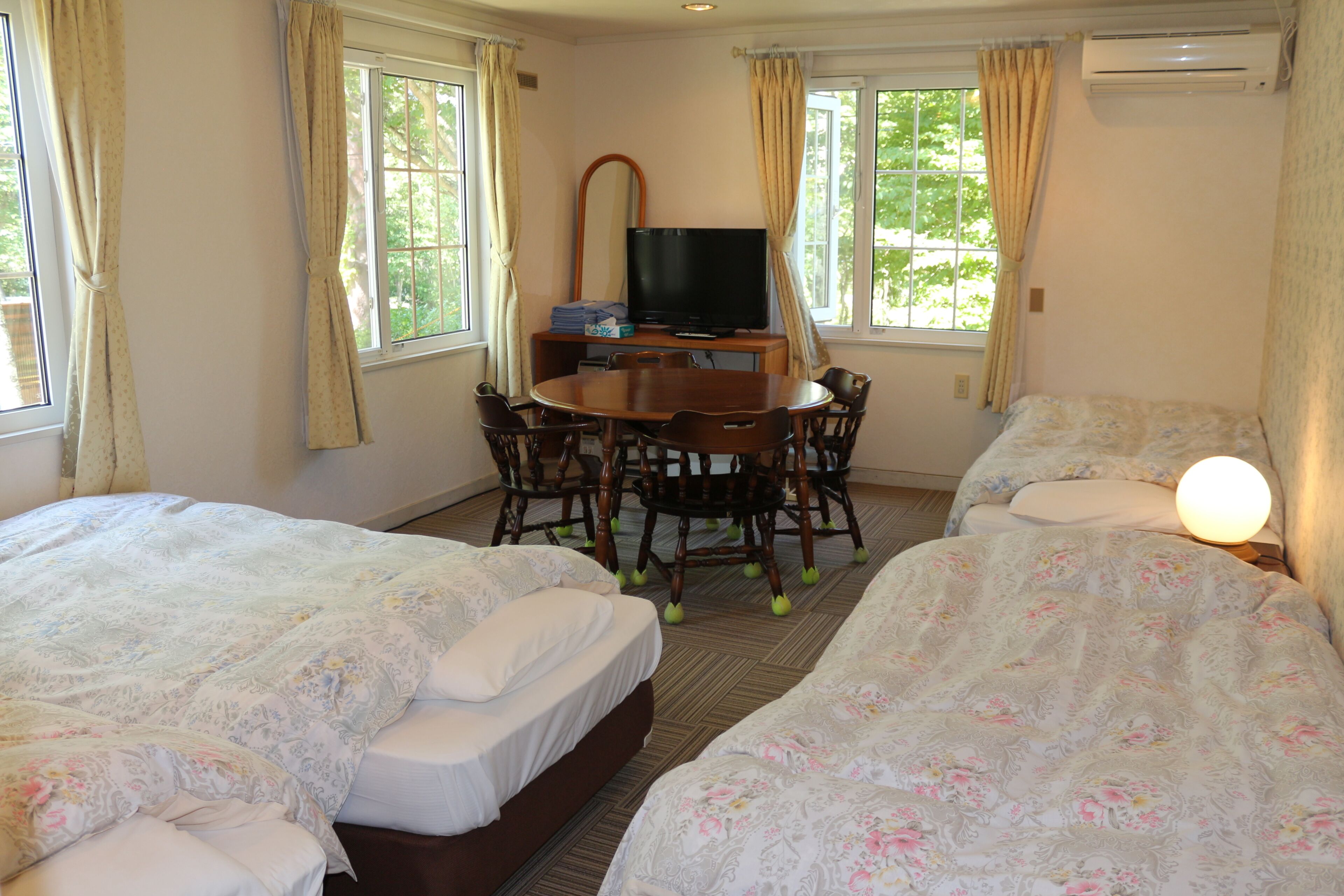 A hotel room with two beds, a dining table with chairs, a television, and a large window.
