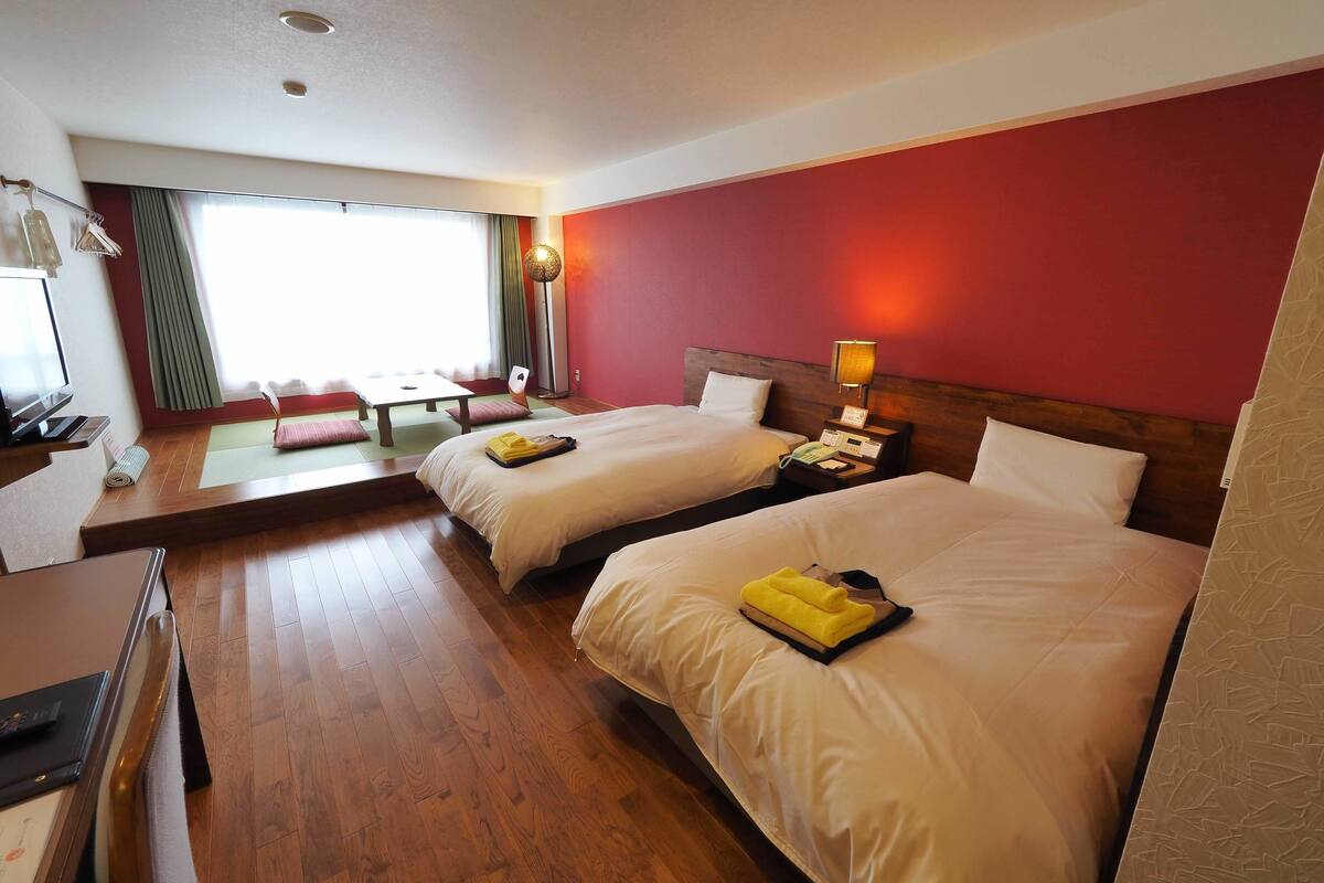 Une chambre d’hôtel avec deux lits, un bureau, une chaise et une fenêtre avec des rideaux.