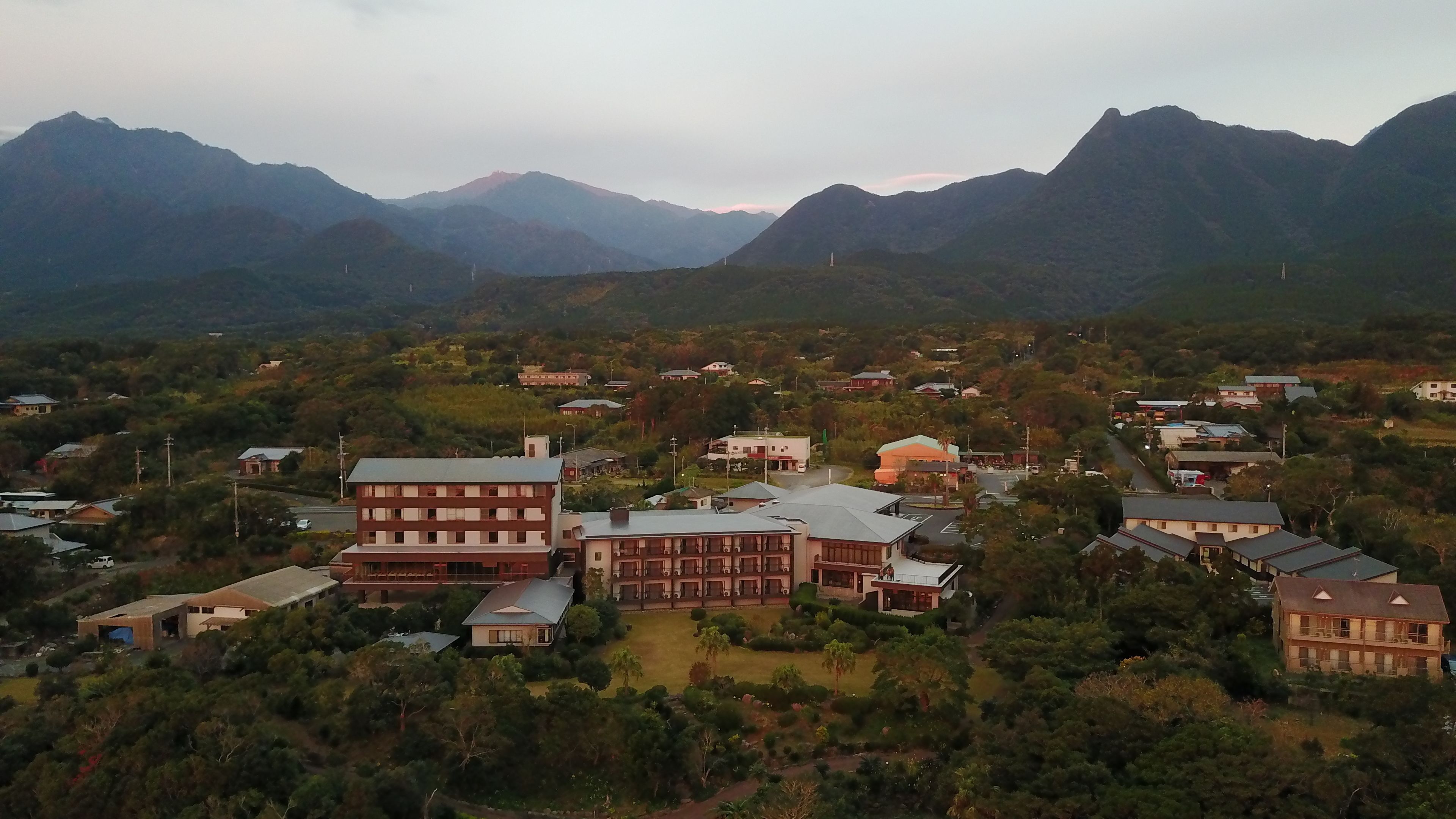 Zona residencial con casas, un edificio grande de varios pisos y montañas al fondo.