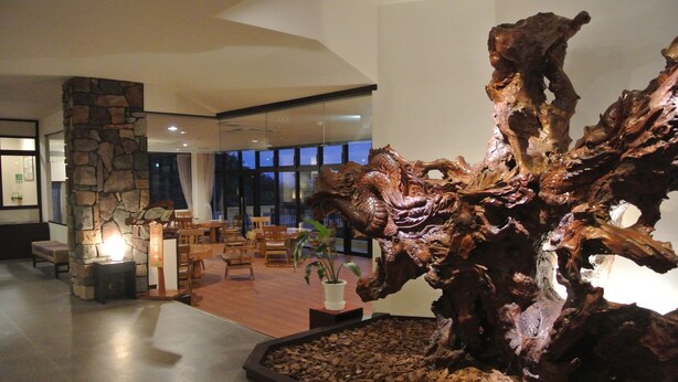 A lobby with a large wooden sculpture, stone pillar, and seating area.