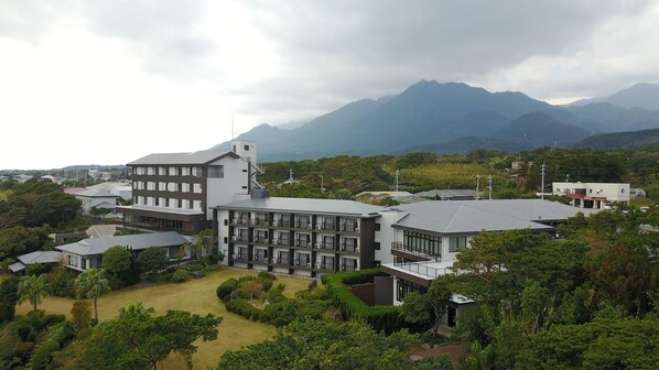 A modern building with multiple floors, surrounded by lush greenery and mountains in the background.